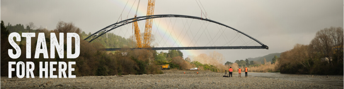 A waterbridge installation over a river with a yellow crane and a rainbow in the background with the words "Stand for here"