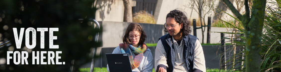 Two people sit outside in the sun looking at a laptop, with the words "Vote for here"