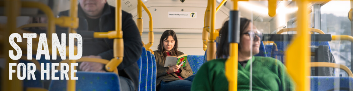 A woman reading a book in the back row of a Metlink bus with the words "Stand for here"